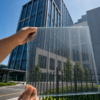 CdTe semi-transparent BIPV glass panel held against modern office building, sky visible through the glass