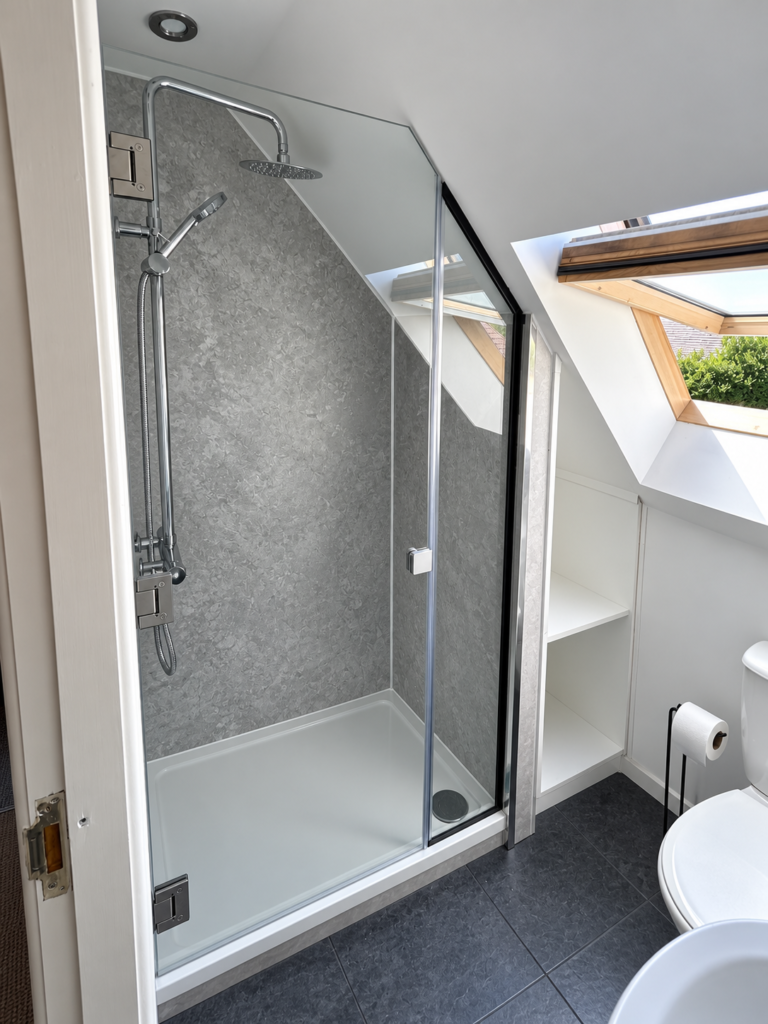 Bespoke glass shower door and shaped side panel beneath a sloping ceiling